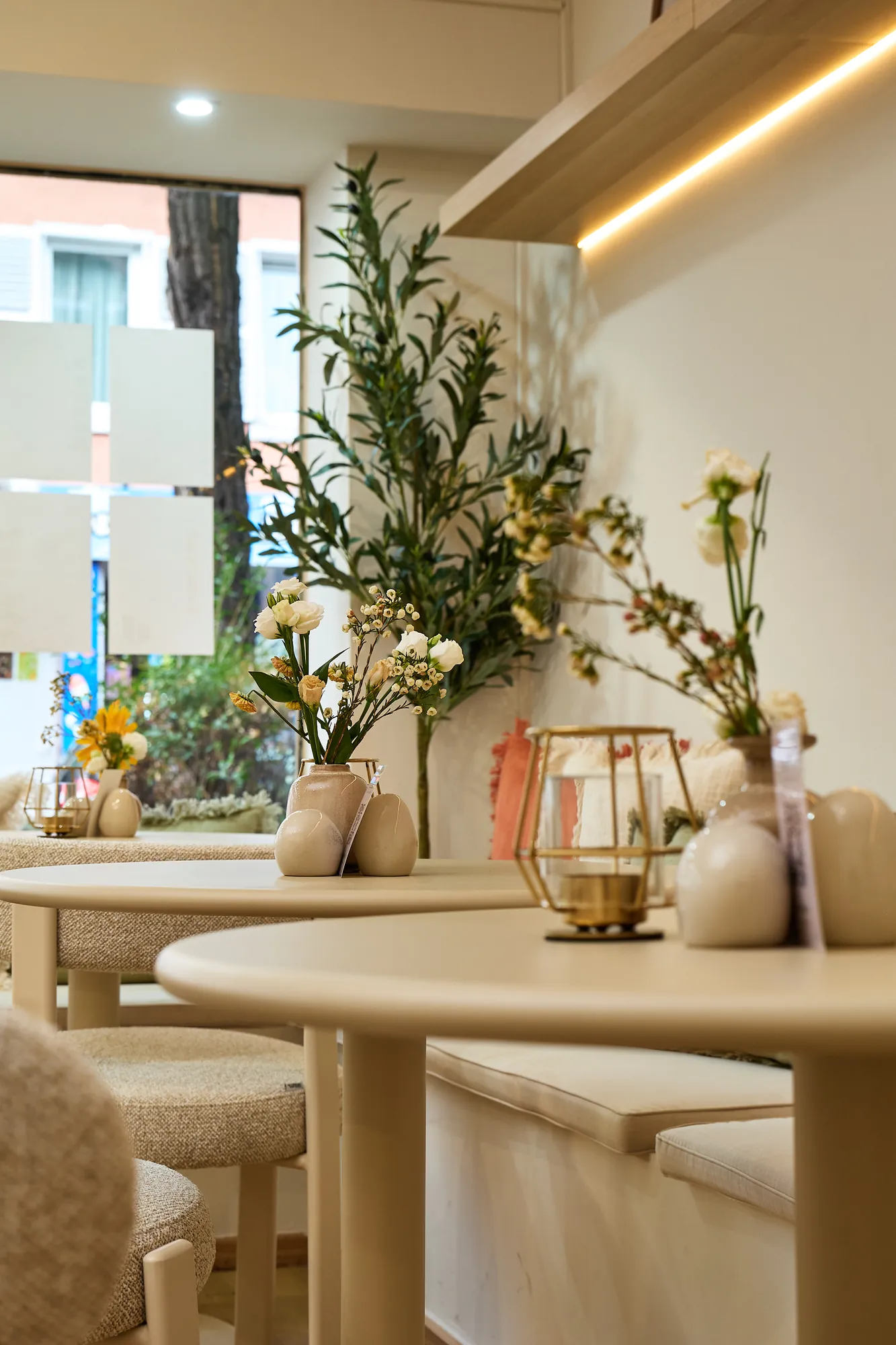 Ein runder Tisch am Fenster im calmá, Kerze und Blumen, dahinter die Sitzbank mit Kissen
